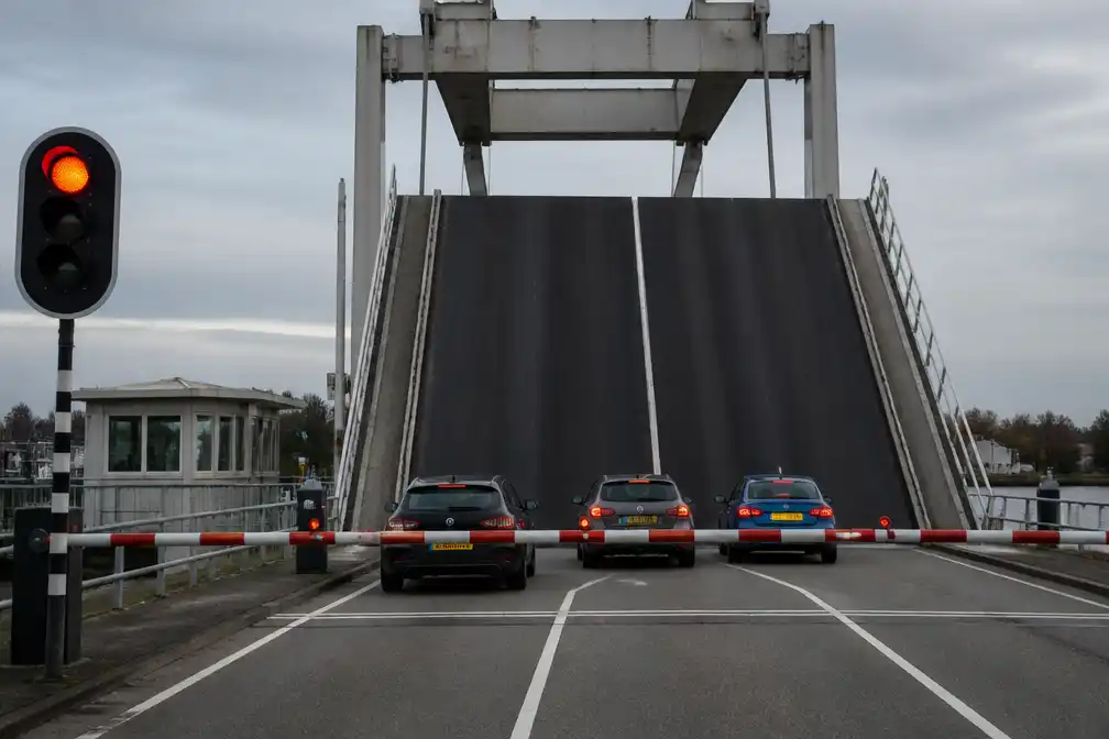 Hefbrug in Waddinxveen omhoog terwijl drie auto's op dek staan; automobilist rijdt eraf